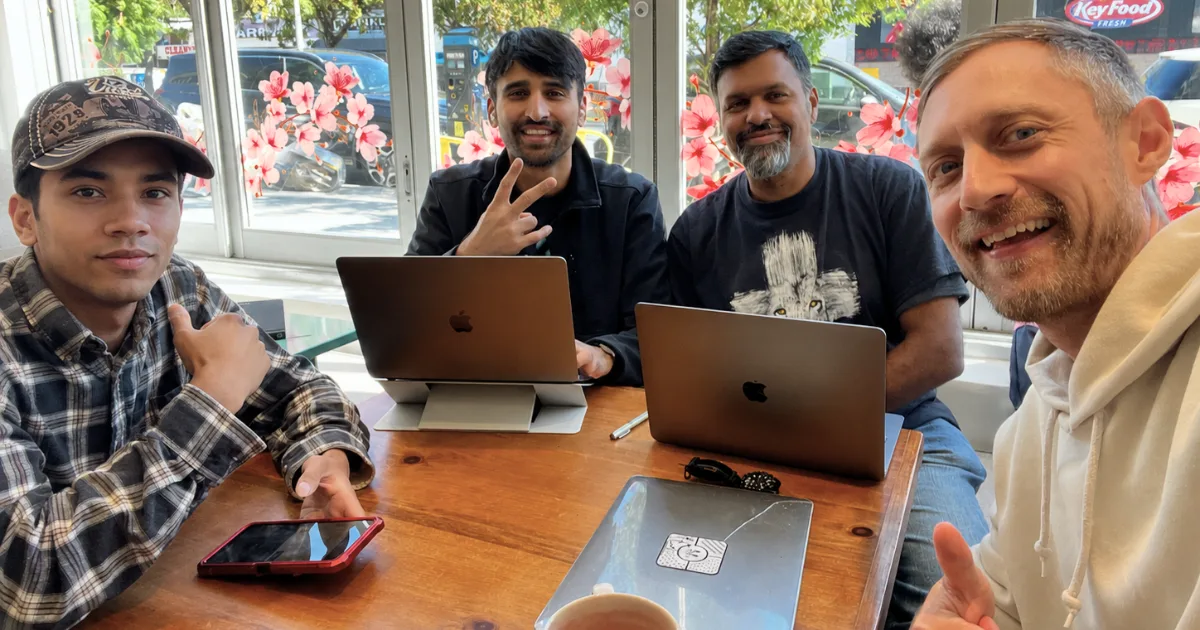 Four people gathered around a café table with laptops open, meeting together to practice.